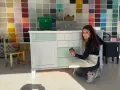 Mujer sonríe mientras trabaja en un mueble, demostrando cómo pintar muebles de madera sin lijar.