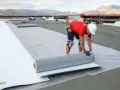 Trabajadores instalan un rollo de material para el aislante térmico exterior en una obra.