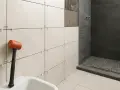 Martillo de goma junto a azulejos listos para alicatar baño. Ducha con azulejos oscuros al fondo.