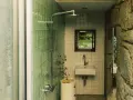 Baños pequeños con ducha, lavabo y espejo con vista a un jardín rocoso. Paredes de azulejos verdes y piedra natural.