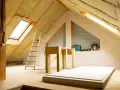 Techo interior en proceso de aislamiento. Se ve el aislante térmico para techos interiores, escalera, materiales de construcción y una ventana de tejado.