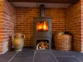 Estufa de leña con fuego encendido, chimenea de ladrillo, leña en cesta y jarrón. Guía para como instalar una estufa de leña con salida horizontal.
