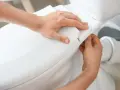 Man's hands carefully fitting the toilet seat, part of the process to como instalar un inodoro al suelo.