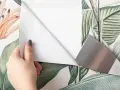 Mano quitando papel pintado floral con espátula.
