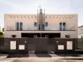 Moderna fachada ventilada de piedra clara con balcones de cristal y rejas oscuras.