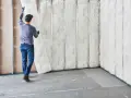 Obrero colocando aislamiento de fibra de vidrio para aislar paredes. El material blanco y esponjoso se inserta entre los montantes metálicos.