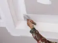 Mano con espátula aplica masilla para reparar techo escayola, dejando un acabado liso y perfecto.
