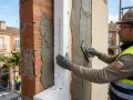 Obrero aplica mortero sobre aislamiento térmico en fachadas. El material SATE mejora la eficiencia energética.