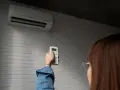 Persona ajusta control remoto de aire acondicionado, pensando en el consumo de la bomba de calor.