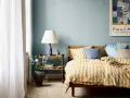 Habitación con paredes azul claro, cama con ropa de cama a rayas amarillas y blancas, y mesita de noche de ratán. Ideas de colores para habitaciones.