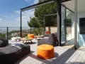 Cómoda terraza ático con sillones y pufs naranjas, vistas a la ciudad y un gran pino.