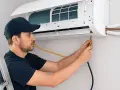 Técnico con gorra azul trabajando en la instalación de un aire acondicionado, conectando mangueras a la unidad interior.