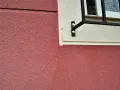 Grietas profundas en pared de color rojo, cerca de una ventana con rejas. Aprende como arreglar grietas profundas en paredes.