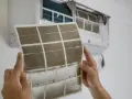 Manos sostienen un filtro de aire acondicionado sucio, mostrando cómo cambiarlo para un aire más limpio.