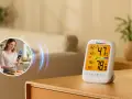 Un higrómetro digital muestra 47% de humedad y 78.9°F. Una mujer sonríe usando su teléfono en la cocina.