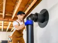 Instalador con guantes azules ensambla tubería negra para chimenea. Guía visual sobre como hacer una chimenea de obra.