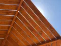 Estructura de madera con tratamiento para exterior, con lamas de madera barnizada bajo un cielo azul brillante.
