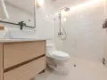 Baño moderno con lavabo sobre mueble de madera, inodoro y ducha con azulejos blancos. ¡Un proyecto de pintar azulejos baño que inspira!