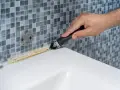 Mano usando una espátula para quitar silicona vieja y sucia de la bañera.