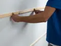 Man placing wooden slats on a white wall, demonstrating como poner listones de madera en la pared.