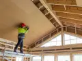 Trabajador en andamio instala paneles aislantes en el techo, parte de un proyecto para como aislar una casa ya construida.