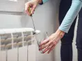 Persona usa un destornillador para purgar aire de un radiador, un paso esencial para limpiar radiadores y optimizar la calefacción.