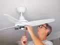 Hombre con gafas ajusta un ventilador de techo pladur con un destornillador.