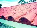 Tejas rojas de barro en un tejado, ideal para reparar tejado sin quitar tejas. Cielo azul y árboles al fondo.