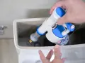 Mano instalando un nuevo mecanismo de descarga para cambiar la cisterna del inodoro.