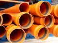 Tubos de PVC naranja apilados, listos para ser instalados en exteriores. Perfectos para proyectos de fontanería y drenaje.