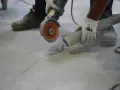 Trabajador usa una amoladora para hacer una solera de hormigón sobre tierra, aspirando el polvo.