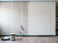 Preparativos para pintar pladur: cinta azul protege el suelo y la pared, cubos de pintura y rodillo listos para transformar la estancia.