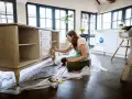 Mujer aplicando una capa de pintura a un mueble antiguo.