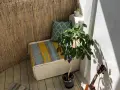 Un rincón acogedor para decorar balcon. Un banco con cojines, planta y luces crea un ambiente relajado.