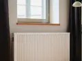 Radiador blanco bajo ventana, con cortinas oscuras y lámpara amarilla. El **calor azul** del invierno se combate con este sistema.
