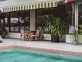 Terraza con piscina y toldo a rayas verdes y blancas. Mesa de madera con sillas de mimbre listas para instalar toldo.