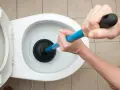 Manos usando un desatascador para como desatascar un water.