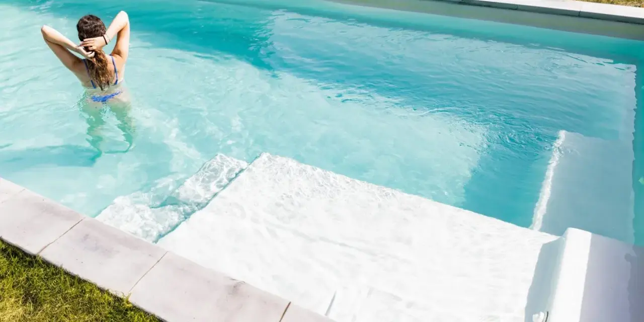 Mujer en bikini azul disfruta de una piscina cristalina, reflejo de un buen mantenimiento de piscinas.
