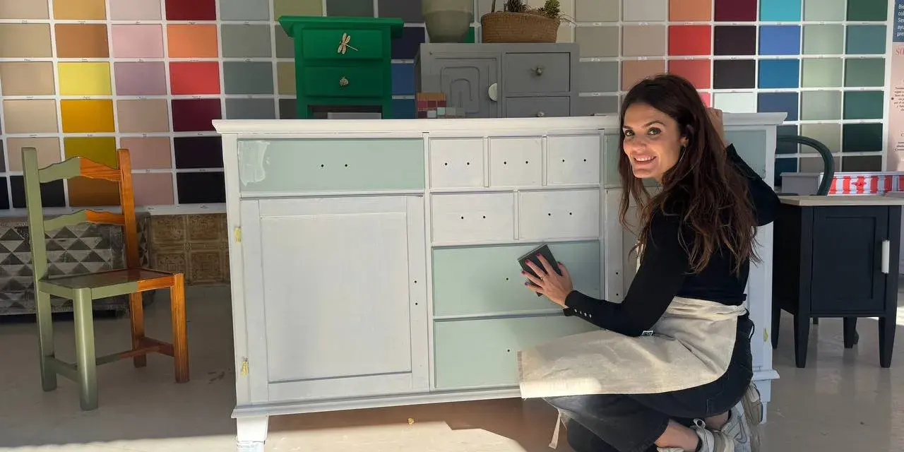 Mujer sonríe mientras trabaja en un mueble, demostrando cómo pintar muebles de madera sin lijar.