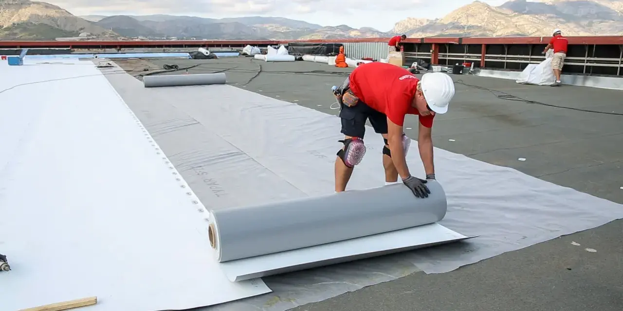 Trabajadores instalan un rollo de material para el aislante térmico exterior en una obra.