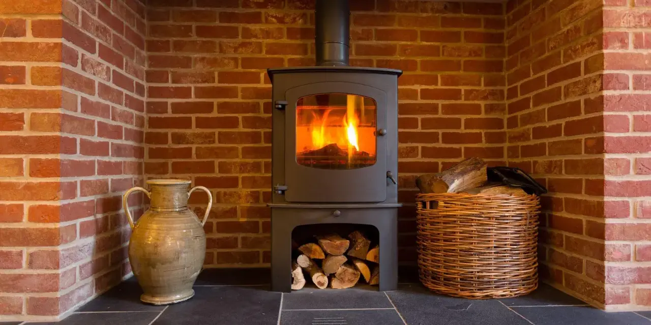Estufa de leña con fuego encendido, chimenea de ladrillo, leña en cesta y jarrón. Guía para como instalar una estufa de leña con salida horizontal.