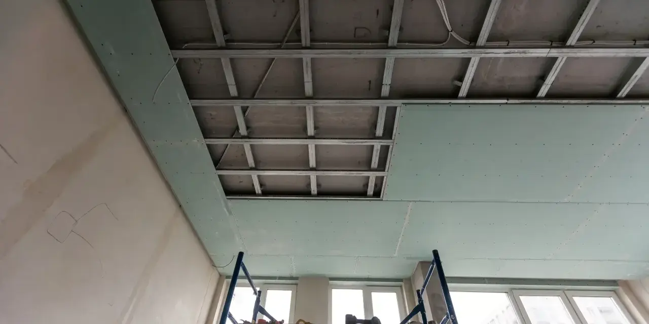 Instalación de falso techo de pladur para insonorizar habitación de ruidos de vecinos. Andamio y estructura metálica visibles.