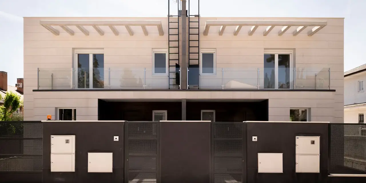 Moderna fachada ventilada de piedra clara con balcones de cristal y rejas oscuras.