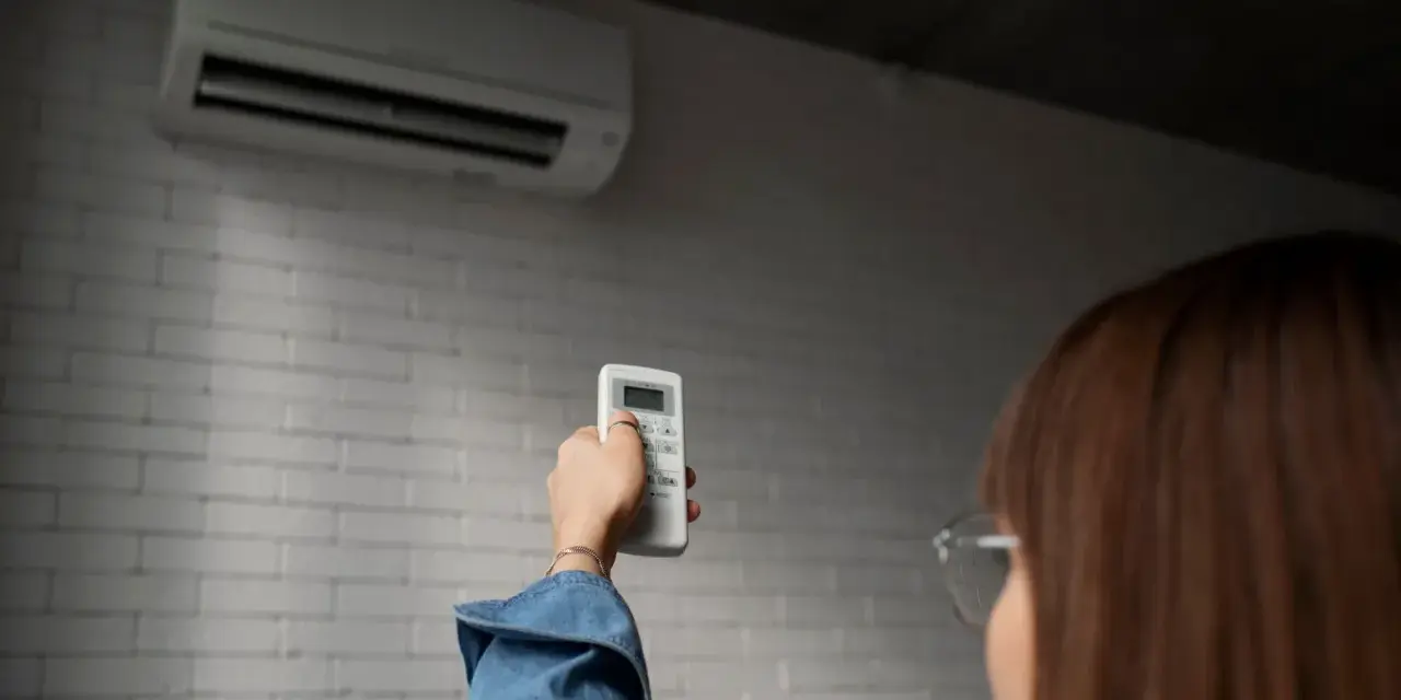 Persona ajusta control remoto de aire acondicionado, pensando en el consumo de la bomba de calor.