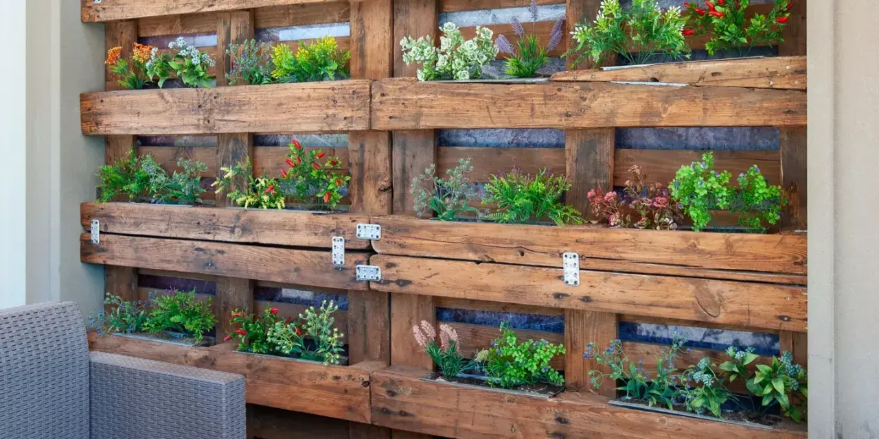 Jardineras con palets crean un jardín vertical lleno de plantas verdes y flores de colores, un oasis en el balcón.