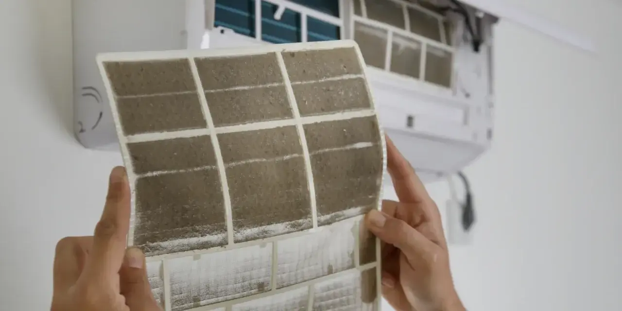 Manos sostienen un filtro de aire acondicionado sucio, mostrando cómo cambiarlo para un aire más limpio.