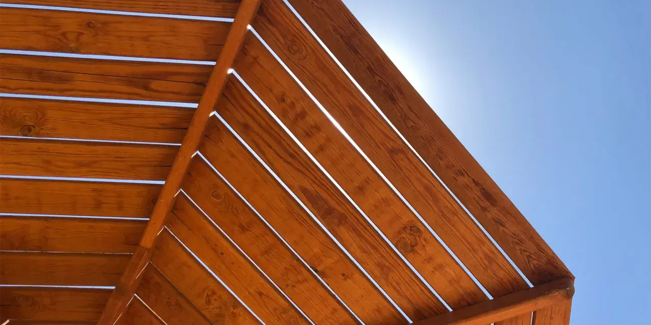 Estructura de madera con tratamiento para exterior, con lamas de madera barnizada bajo un cielo azul brillante.