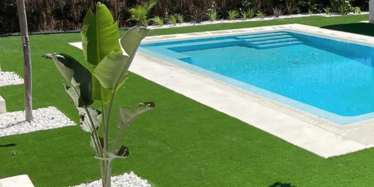 Jardín moderno con piscina y césped artificial. La colocación de césped artificial realza la belleza del espacio.