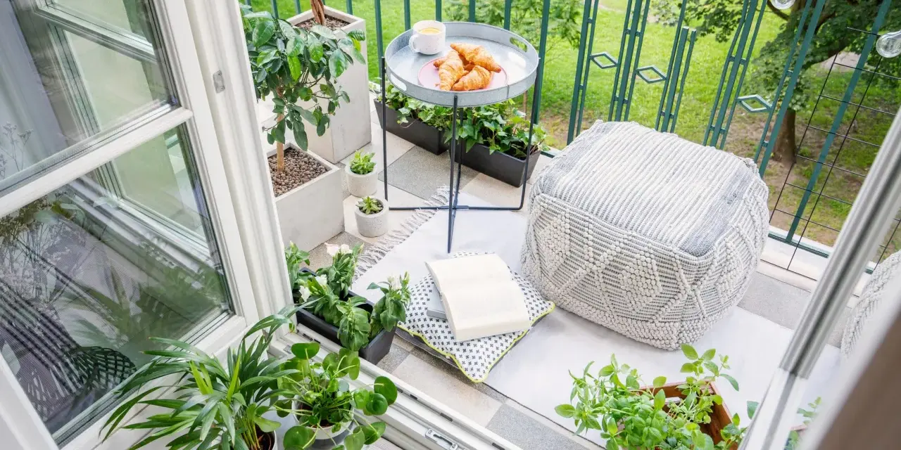 Acogedor rincón en unas terrazas pequeñas con encanto: cojines, plantas, un libro y cruasanes para un desayuno perfecto.