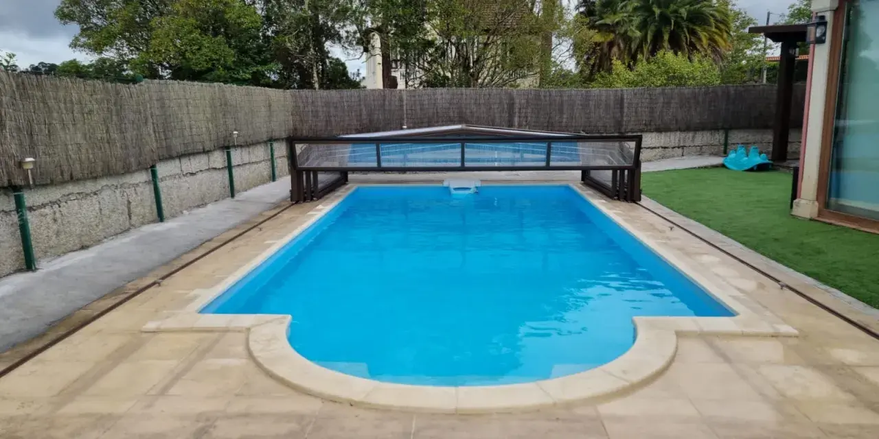 Piscina con cubierta retráctil, rodeada de césped artificial y un sistema para canalizar agua de lluvia.
